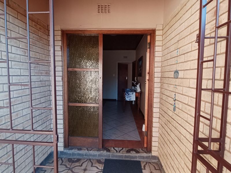 Entrance area featuring a brick facade, security gate, and a timber-framed glass door leading into the home's interior hallway.