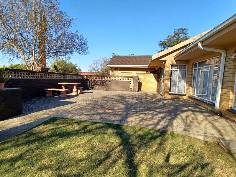 Spacious paved rear patio area featuring a built-in braai, brick boundary walls, and direct access to the home through large windows.