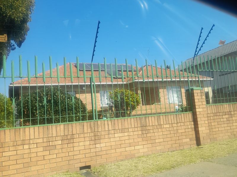 Front view of a brick house featuring a secure boundary wall with electric fencing and roof-mounted solar panels.