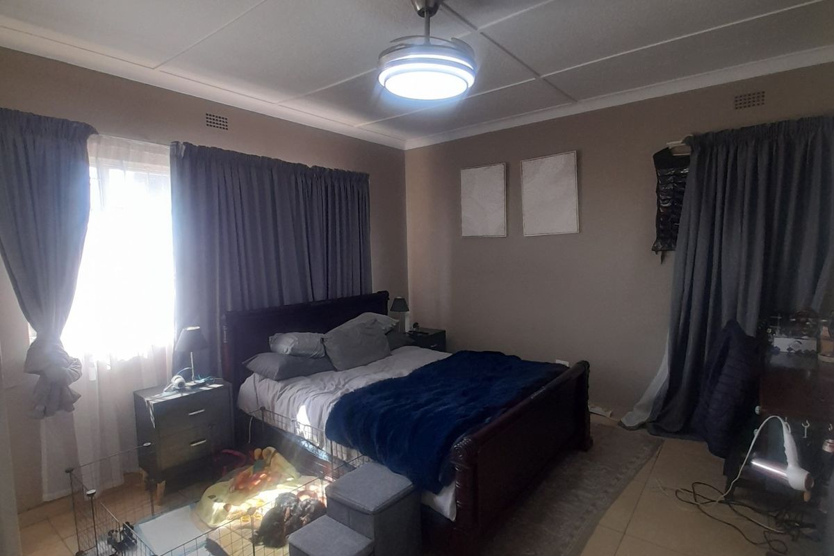 A spacious bedroom featuring tiled flooring, a central ceiling fan, and neutral wall tones, offering a comfortable and functional living space.