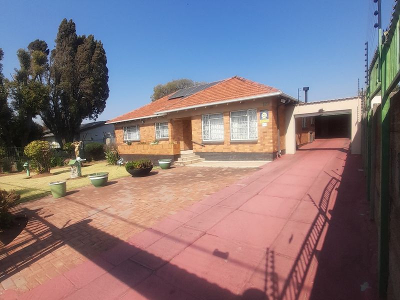 Front view of a single-story brick house featuring a tiled roof, paved driveway, attached garage, and perimeter electric fencing.