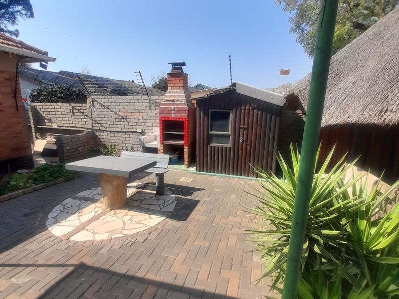 Outdoor patio area featuring a built-in brick braai, paved flooring, and a shade cloth canopy, adjacent to a timber storage shed.