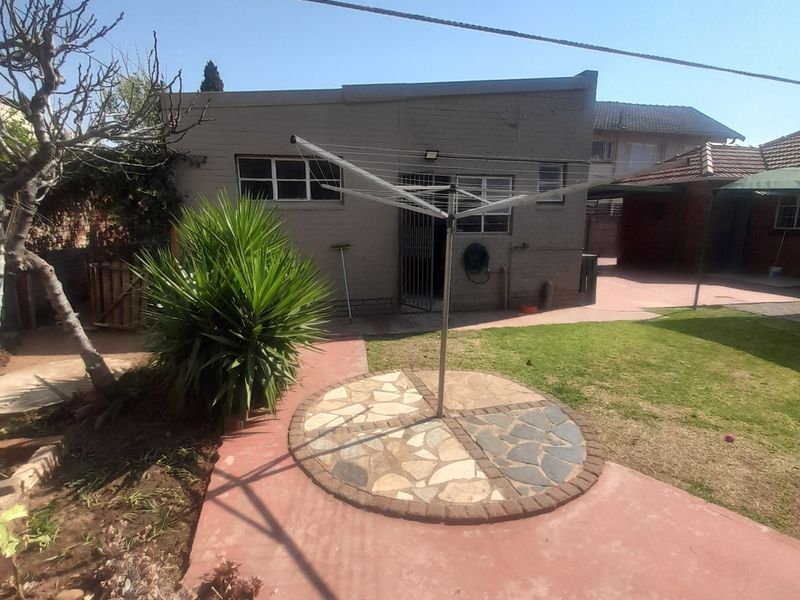 Rear exterior view of the property featuring a paved patio area, lawn, and brick building facade.