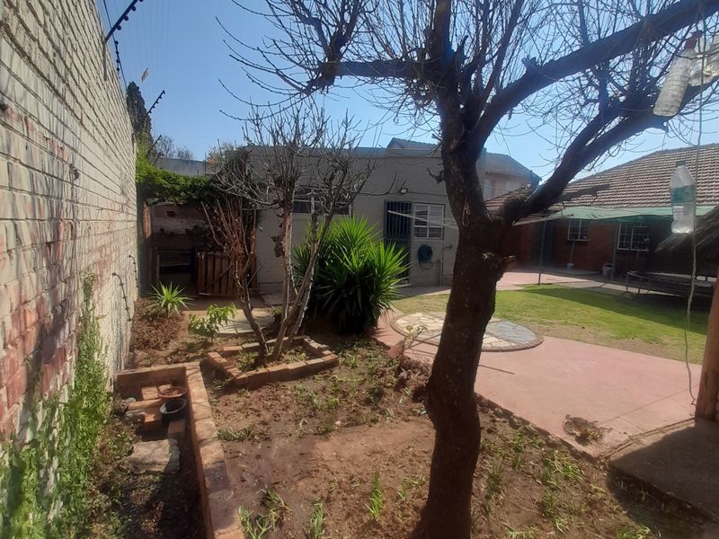Rear garden area featuring a paved patio, lawn, brick planter beds, and perimeter wall with electric fencing.