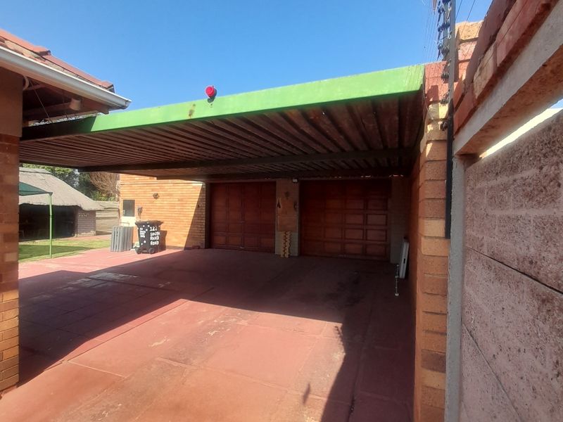 A double garage with an attached carport, featuring brick construction, paved driveway, and perimeter electric fencing.