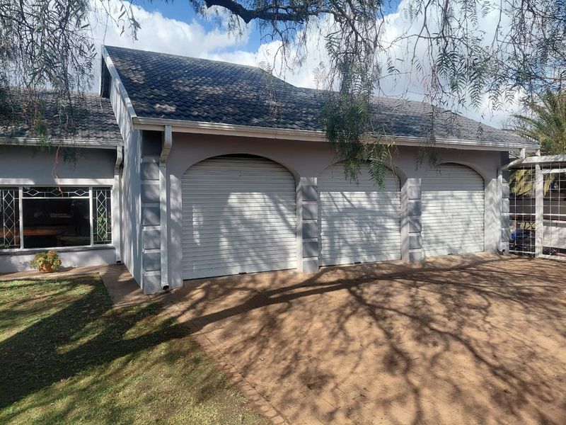 A well-maintained triple garage featuring roller shutter doors, a tiled roof, and a paved driveway entrance.
