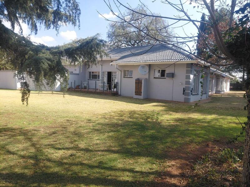 Rear view of the house featuring a tiled roof, a small patio area with railings, and a spacious surrounding lawn.