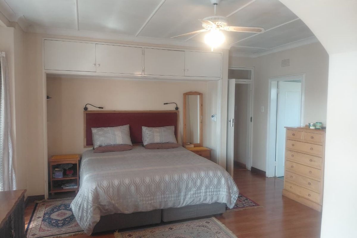 Spacious bedroom featuring laminate flooring, a ceiling fan, and extensive built-in cupboard storage surrounding the bed area.