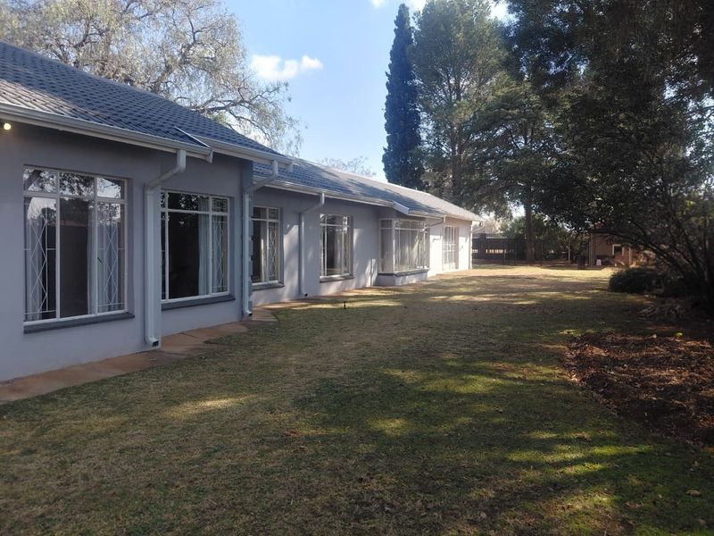 Rear view of the house featuring a tiled roof, large windows with security bars, and a spacious lawn area.