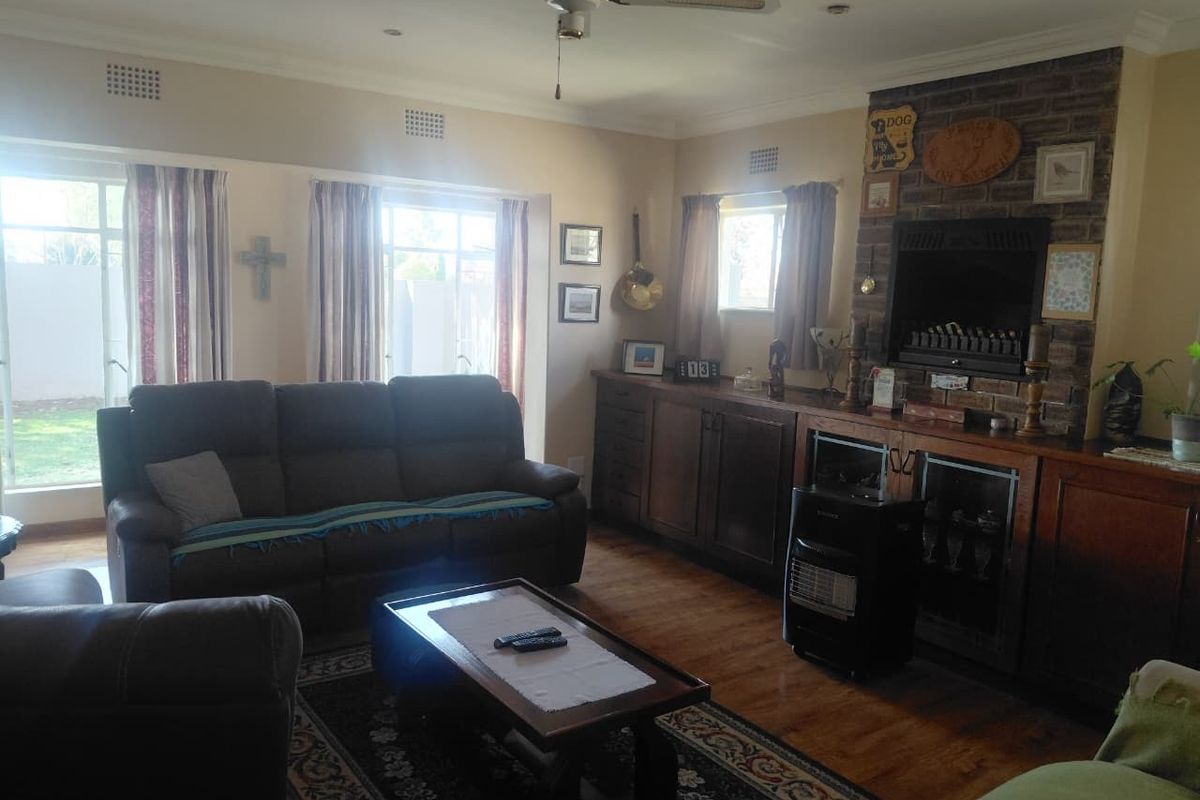 Spacious living room featuring a brick fireplace, custom built-in cabinetry, hardwood flooring, and large windows providing natural light.