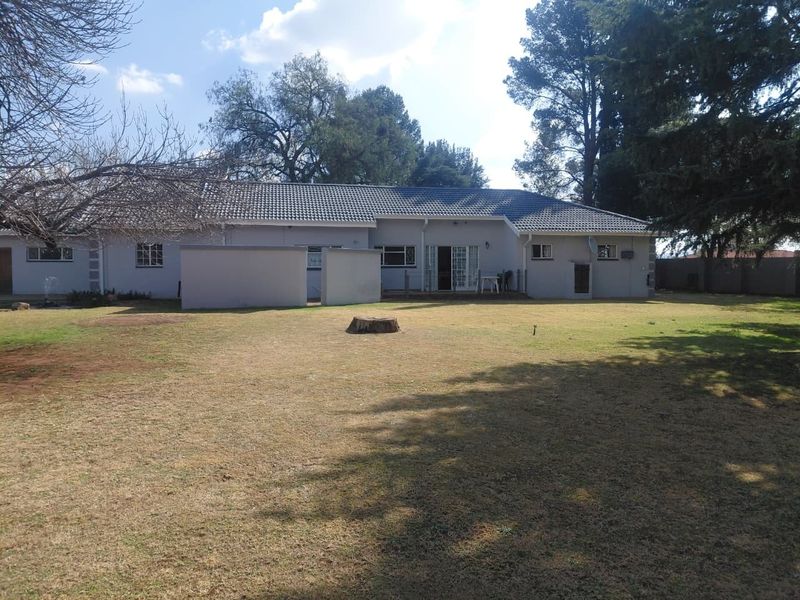 Rear view of the house featuring a tiled roof, sliding door access, and a spacious backyard with established trees and perimeter walling.