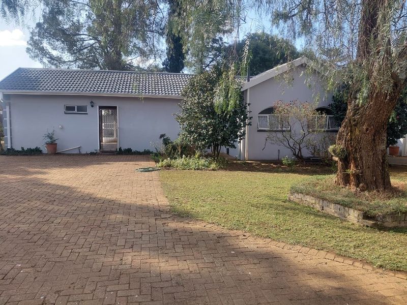Front view of the property featuring a paved driveway, landscaped garden with mature trees, and a well-maintained exterior facade.