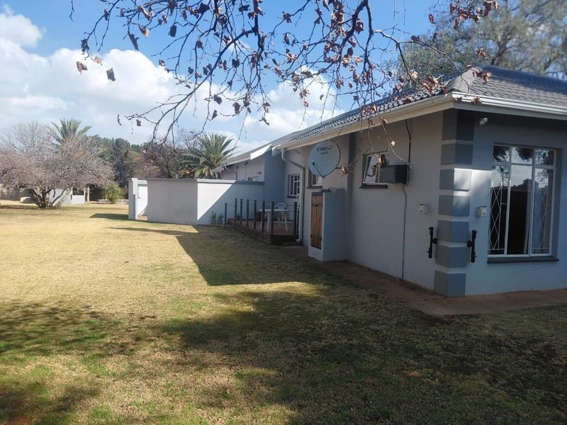Rear view of the house featuring a tiled roof, security bars on windows, and a satellite dish, set against a spacious garden area.