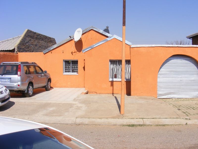 Front elevation of a single-story house featuring a concrete driveway, security bars on windows, and an integrated garage with a metal roller door.