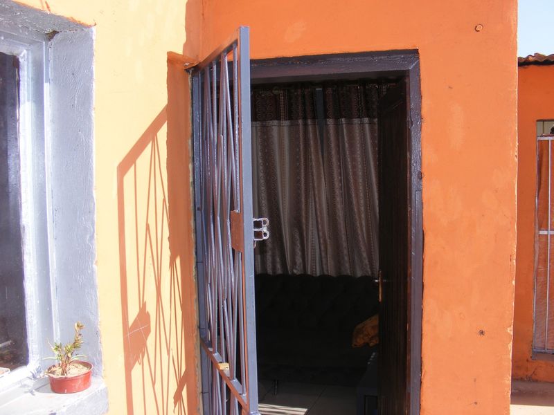 Exterior view of an entrance featuring a metal security gate and a timber door frame set against an orange painted wall.