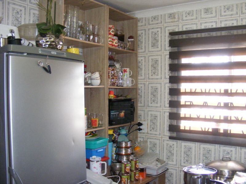 A kitchen corner featuring built-in shelving units and patterned wall tiles, providing functional storage space with a window fitted with a modern roller blind.