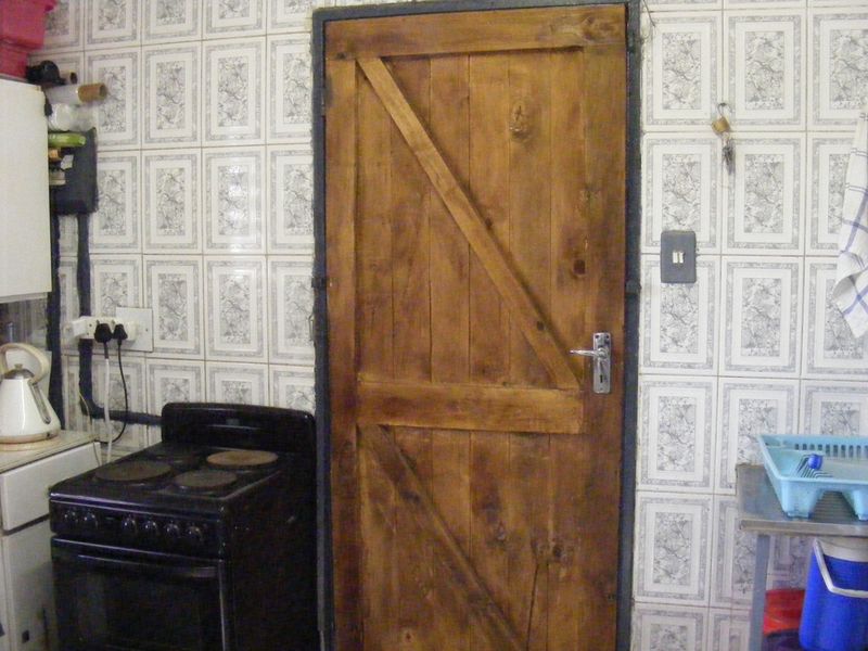 A kitchen area featuring dated wall tiles, a rustic wooden door, and a freestanding electric stove.