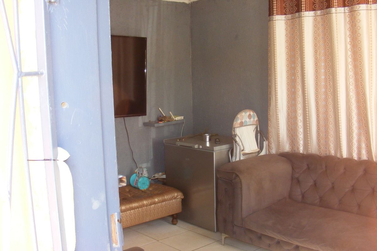 A living room area featuring tiled flooring and a wall-mounted television, requiring cosmetic updates to the wall finishes.