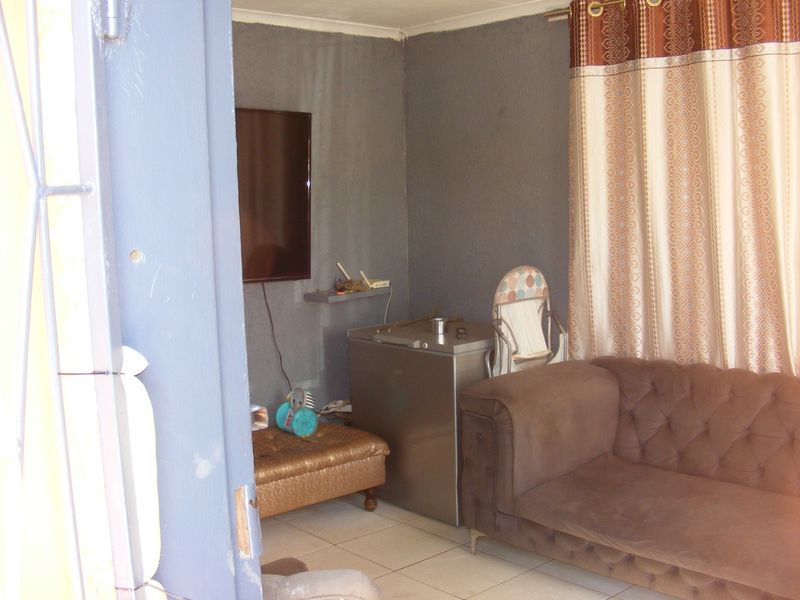 A living room area featuring tiled flooring and a wall-mounted television, requiring cosmetic updates to the wall finishes.