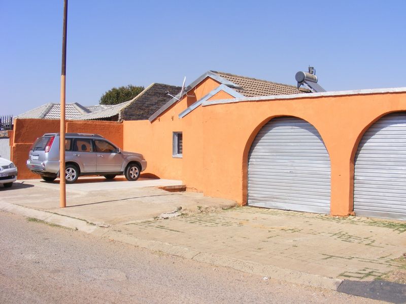 Front exterior view of the property featuring a double garage with roller shutter doors, paved driveway, and a solar water heating system.