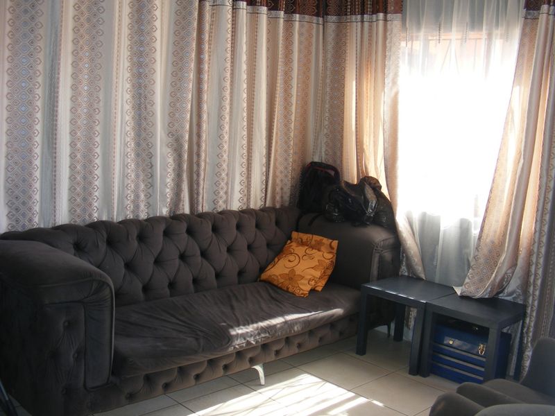 A living room area featuring tiled flooring and natural light from a window with floor-to-ceiling curtains.