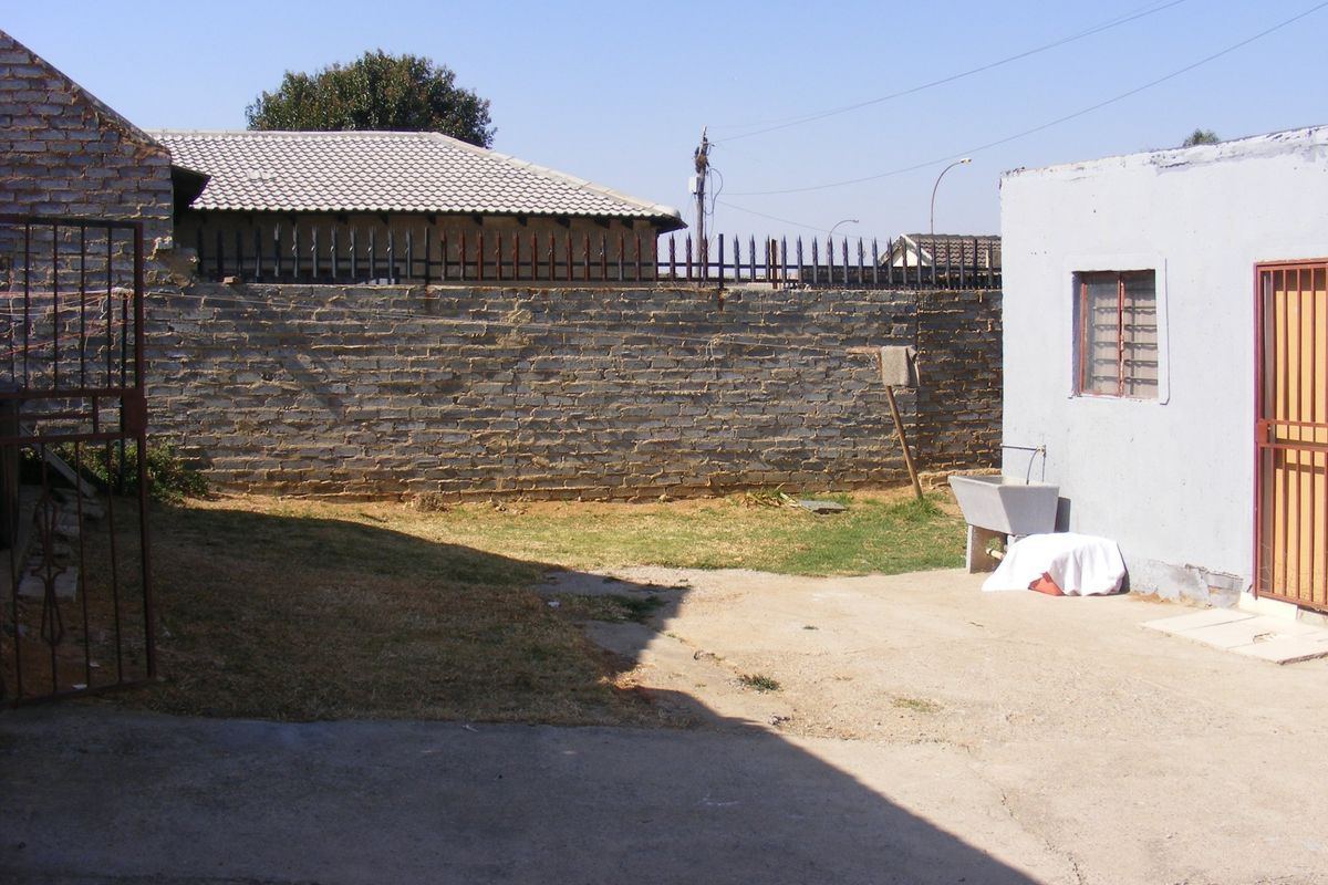 Rear yard area featuring a concrete apron, brick boundary wall with security spikes, and an external utility sink.