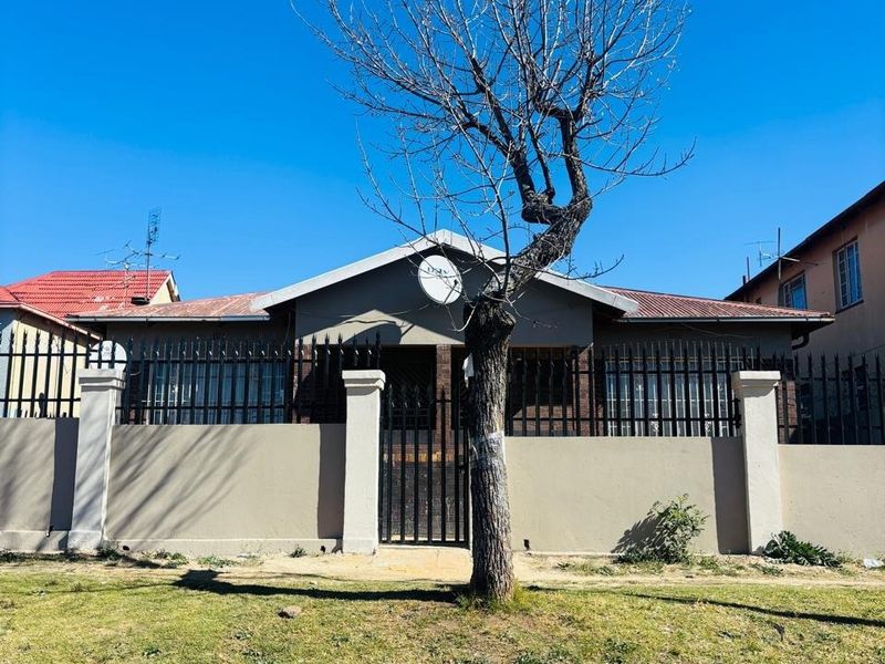 Front view of a residential house featuring a secure perimeter wall with metal fencing and a gated entrance.