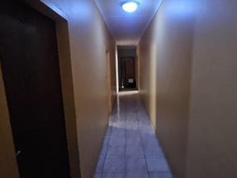A simple, tiled interior hallway connecting multiple rooms, featuring neutral wall tones and overhead lighting.