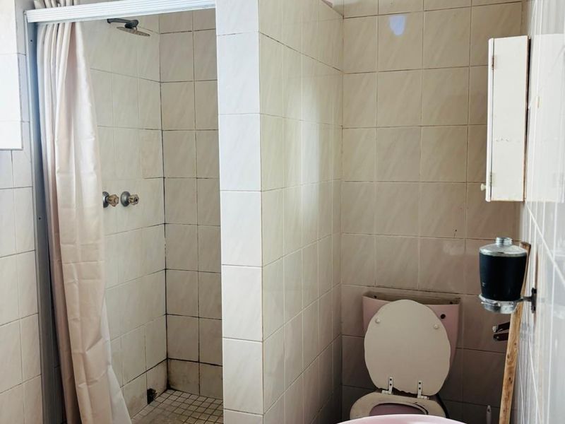A dated bathroom featuring a shower enclosure, pedestal basin, and toilet with original tiled finishes, requiring modernization to improve aesthetic appeal.