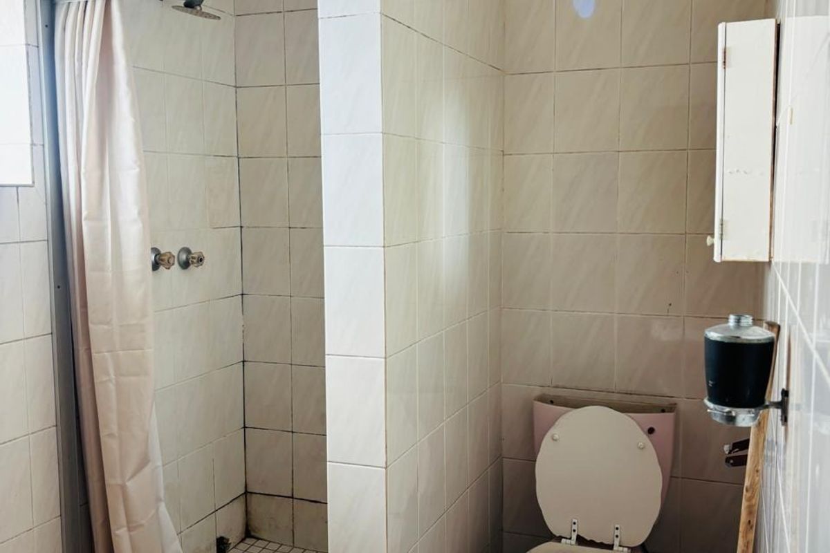 A dated bathroom featuring a shower enclosure, pedestal basin, and toilet with original tiled finishes, requiring modernization to improve aesthetic appeal.