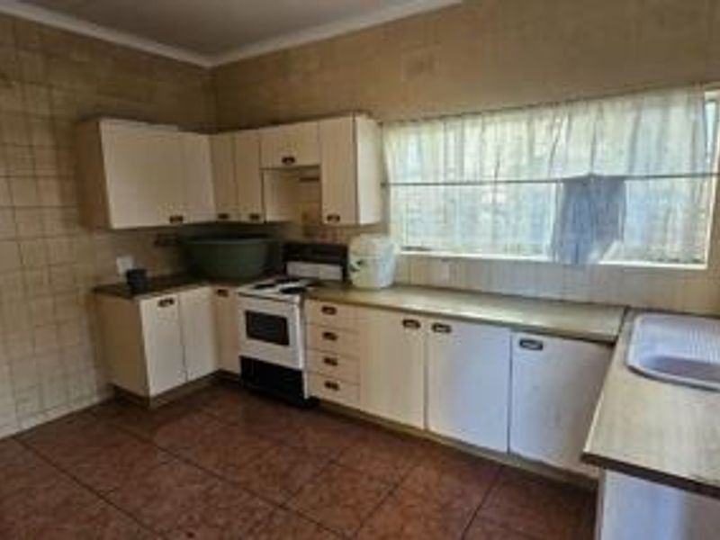 A dated kitchen featuring original cabinetry, tiled walls and floors, and a functional layout with a stainless steel sink and freestanding stove.