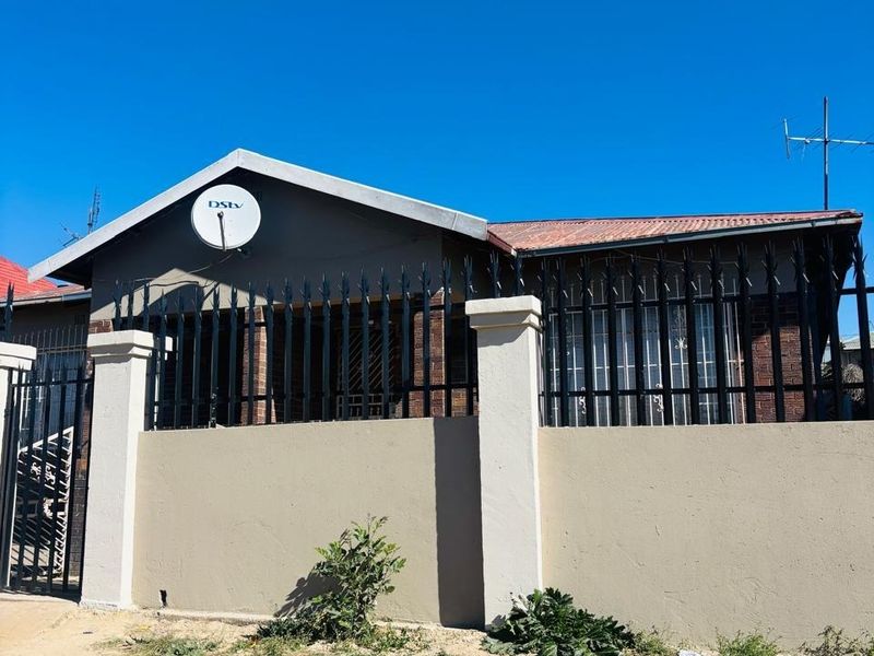 Front exterior view of a residential house featuring a perimeter wall, metal security fencing, and a tiled roof.