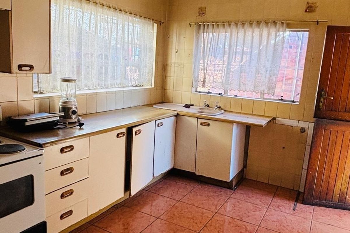 A dated kitchen featuring original cabinetry, tiled walls, and flooring, offering significant potential for a modern renovation and layout update.