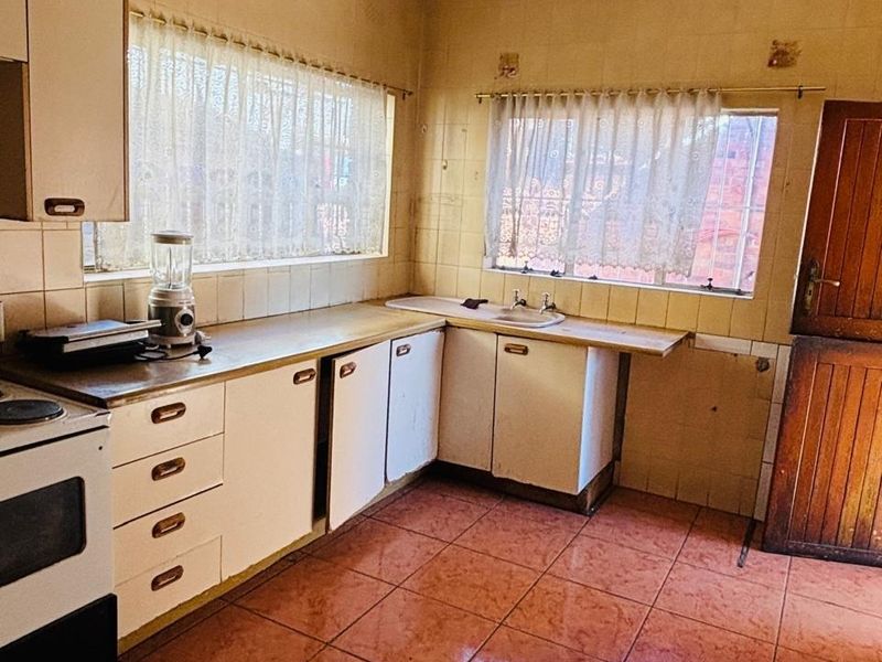 A dated kitchen featuring original cabinetry, tiled walls, and flooring, offering significant potential for a modern renovation and layout update.