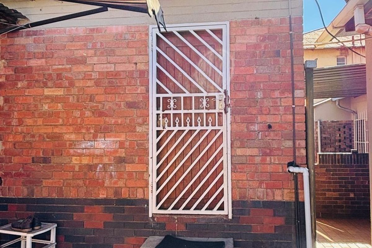 Rear exterior view featuring a brick facade, a security gate entrance, concrete steps, and a retractable awning over a paved courtyard area.