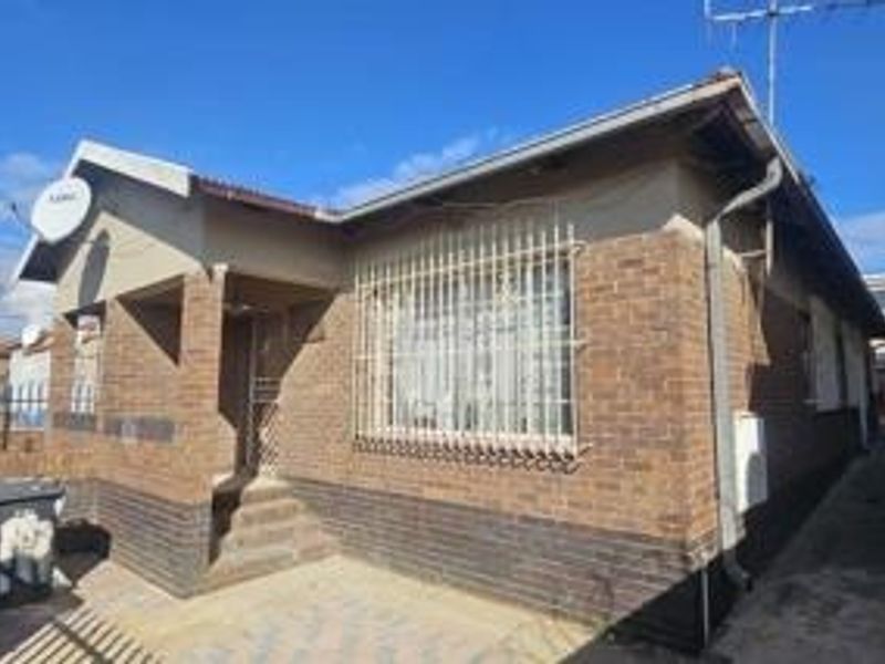 Front elevation of a single-story brick house featuring security bars on windows and a paved entrance area.
