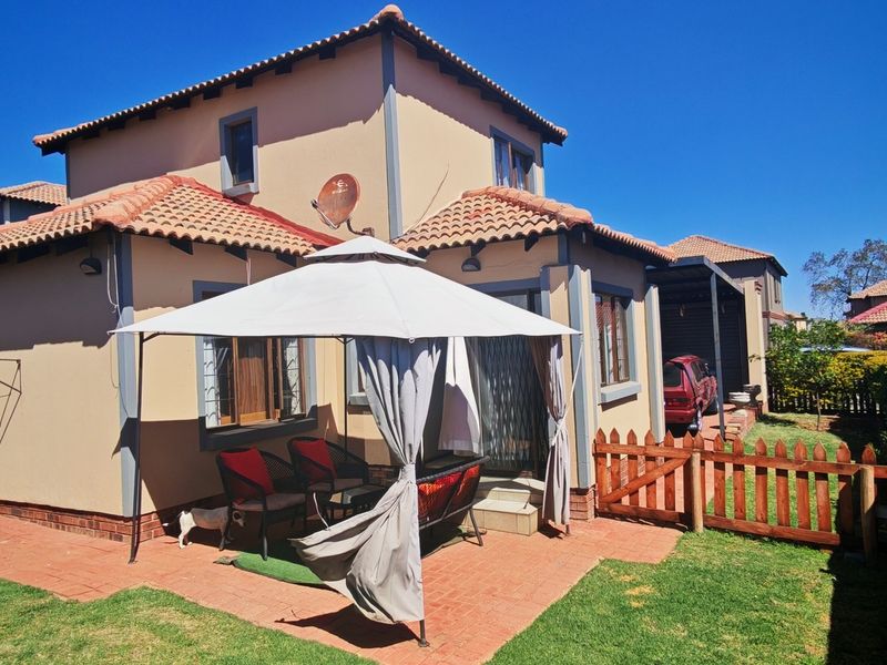 Rear view of the house featuring a paved patio area, terracotta tiled roof, and a wooden picket fence enclosing the garden.