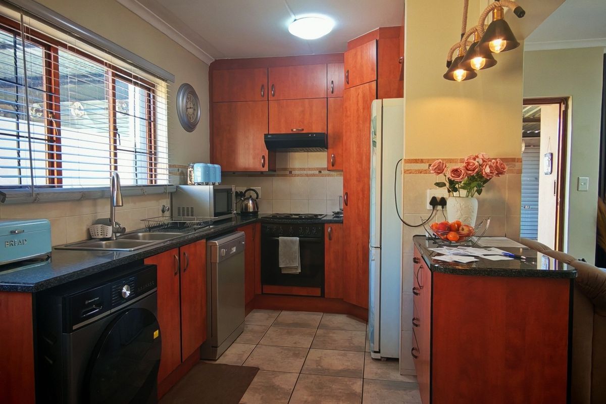 A functional kitchen featuring wood-finish cabinetry, granite countertops, a double basin sink, and built-in cooking appliances, seamlessly flowing into the adjacent living area.