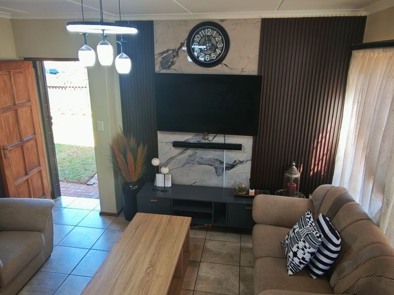 A comfortable living room featuring tiled flooring, a decorative feature wall with integrated media space, and direct access to the exterior.
