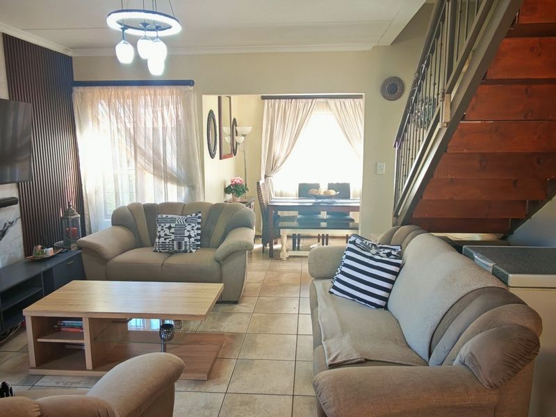 Open plan living and dining area featuring tiled flooring, a wooden staircase with metal railing, and a decorative feature wall.