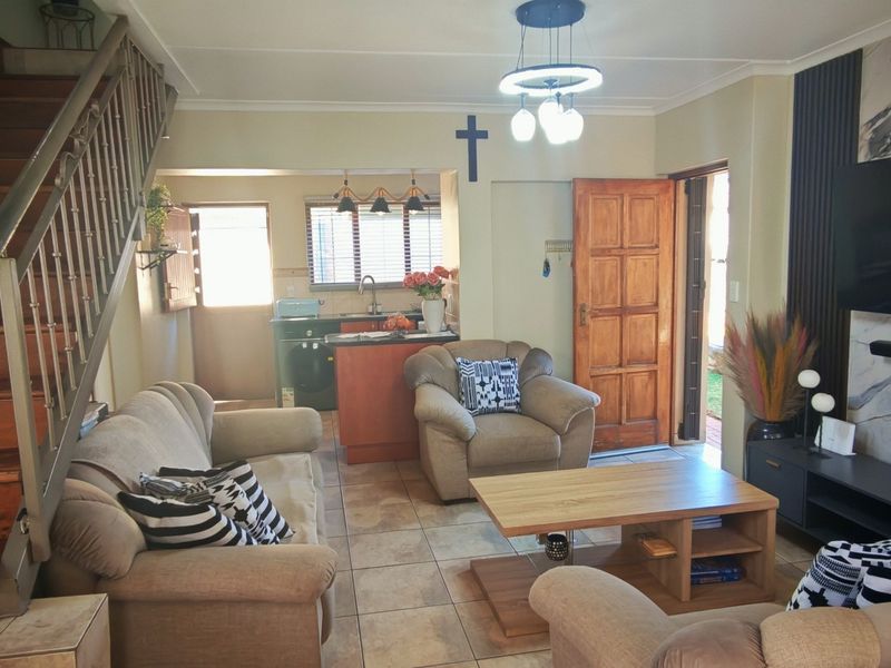 Open plan living area featuring a wooden staircase, tiled flooring, and a compact kitchen space with direct access to the exterior.