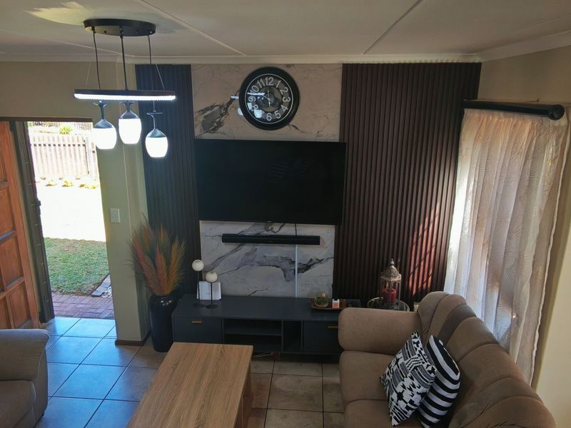 A well-maintained living room featuring a modern feature wall with marble-look cladding, vertical timber paneling, and tiled flooring with direct access to the exterior.