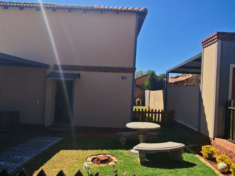 A private rear garden area featuring a paved patio, small lawn, and secure boundary walling with a covered carport structure.