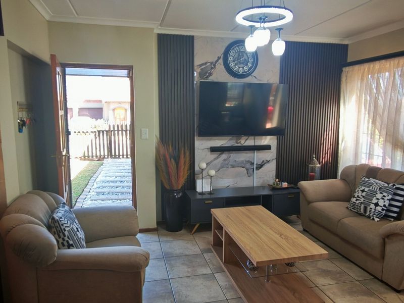 A well-maintained living room featuring a stylish feature wall with vertical slats and marble-look paneling, complemented by neutral tiled flooring and modern lighting.
