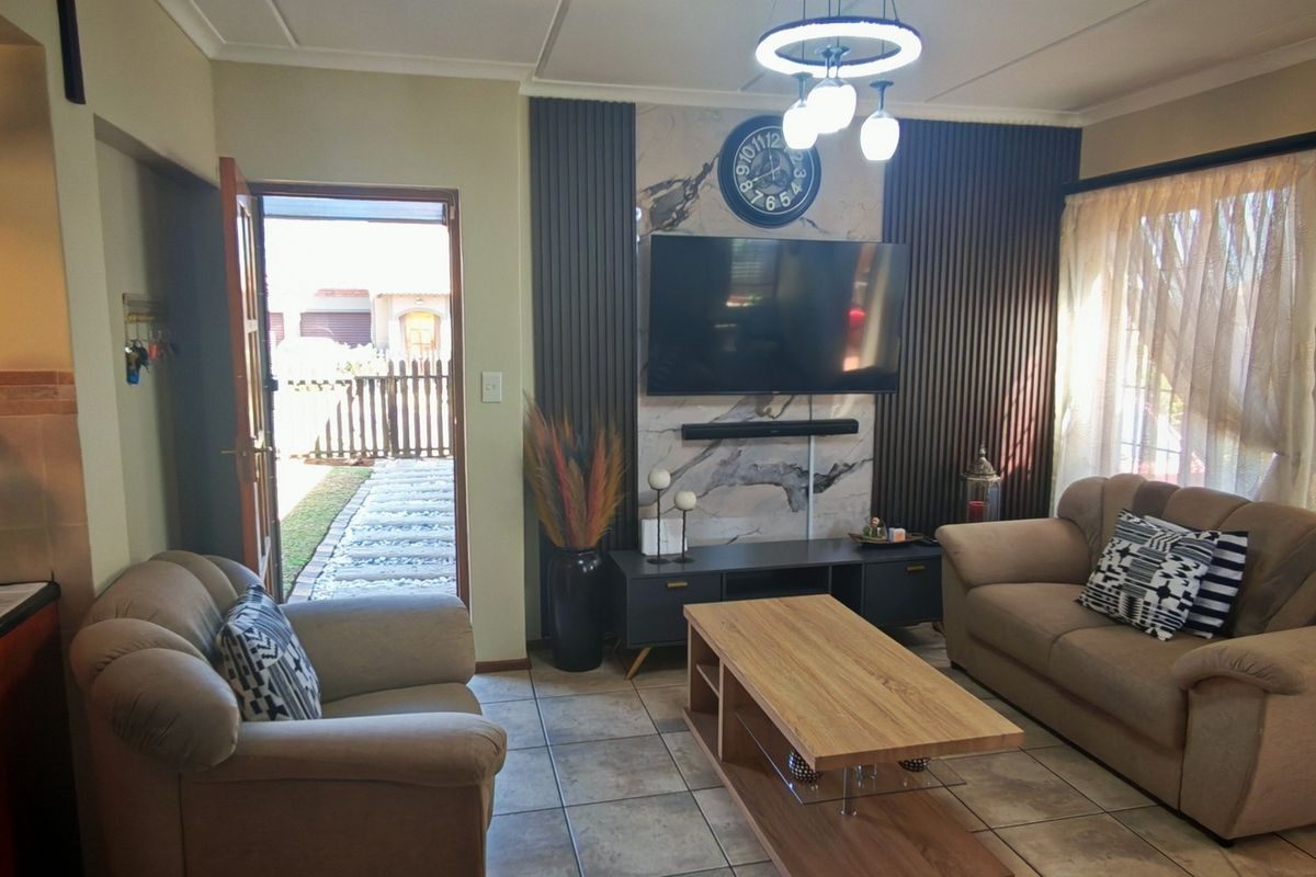 A well-maintained living room featuring a stylish feature wall with vertical slats and marble-look paneling, complemented by neutral tiled flooring and modern lighting.
