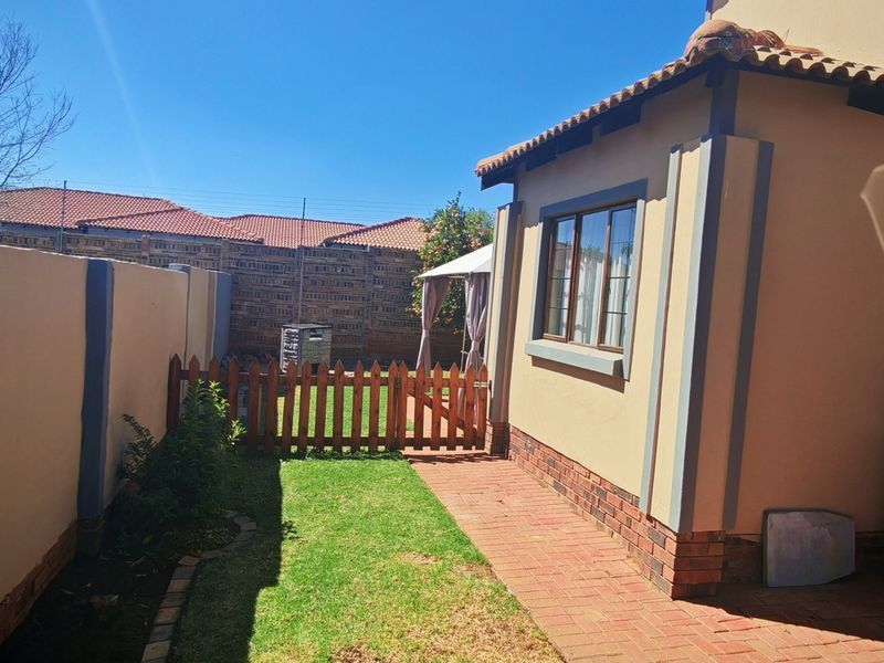 A view of the rear exterior area featuring a brick-paved walkway, a small lawn, and a wooden gate leading to the garden space.
