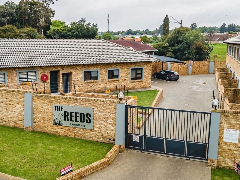 Aerial view of the townhouse complex entrance featuring a secure gated access, face brick facade, paved driveway, and perimeter wall with electric fencing.