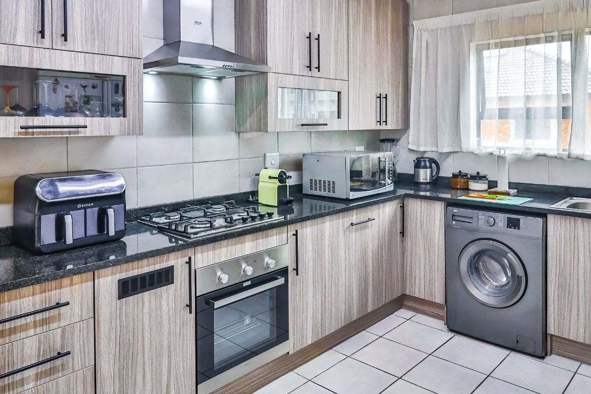 A functional kitchen featuring wood-grain cabinetry, granite countertops, a gas hob, an electric oven, and a built-in washing machine.