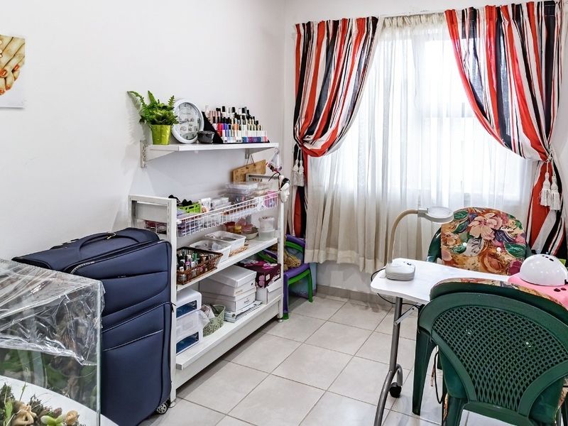 A functional bedroom space currently utilized as a home workspace, featuring tiled flooring and window treatments.
