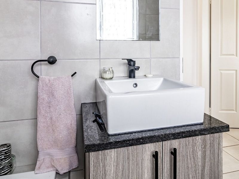 A modern bathroom vanity featuring a white vessel sink, black faucet, granite countertop, and wood-grain cabinetry with contemporary black hardware.